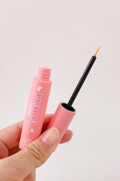 Pink eyeliner pencil with brush held by a hand against a light gray background