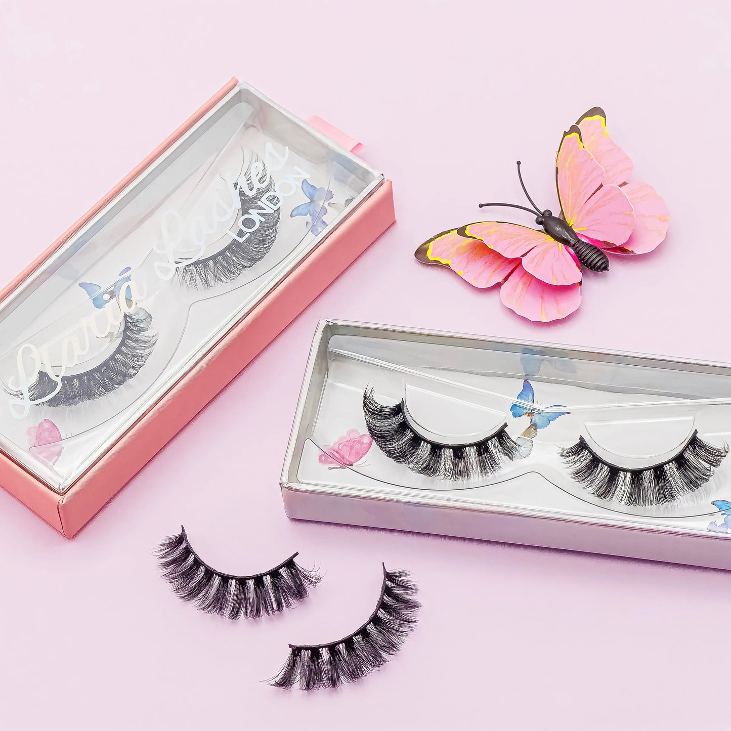 False eyelashes in open boxes with a pink butterfly on a pink background