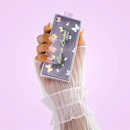 Hand holding a decorative makeup product with 'Lila Lashes' branding against a light purple background
