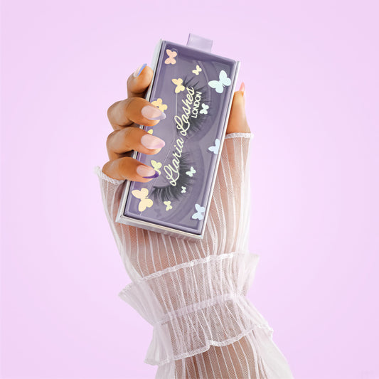 Hand holding a decorative makeup product with 'Lila Lashes' branding against a light purple background
