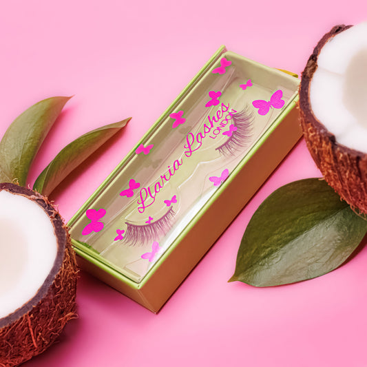 Box of false eyelashes with coconut halves and leaves on a pink background