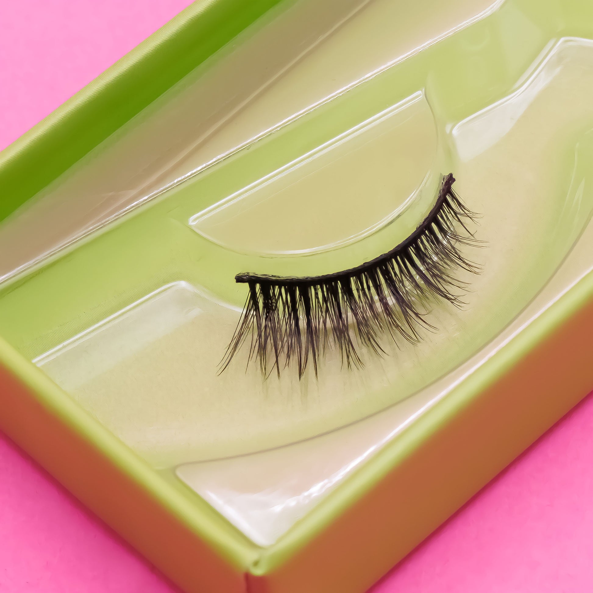 False eyelashes in a green and clear case on a pink background