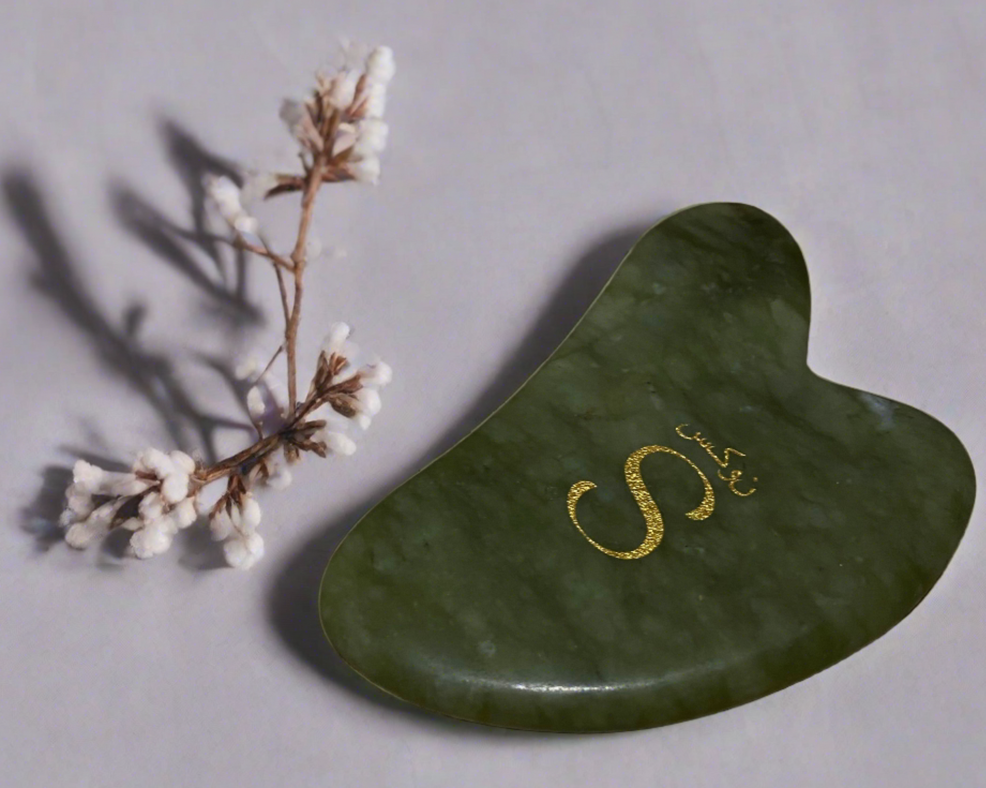 Green gua sha tool with gold lettering on a light gray background