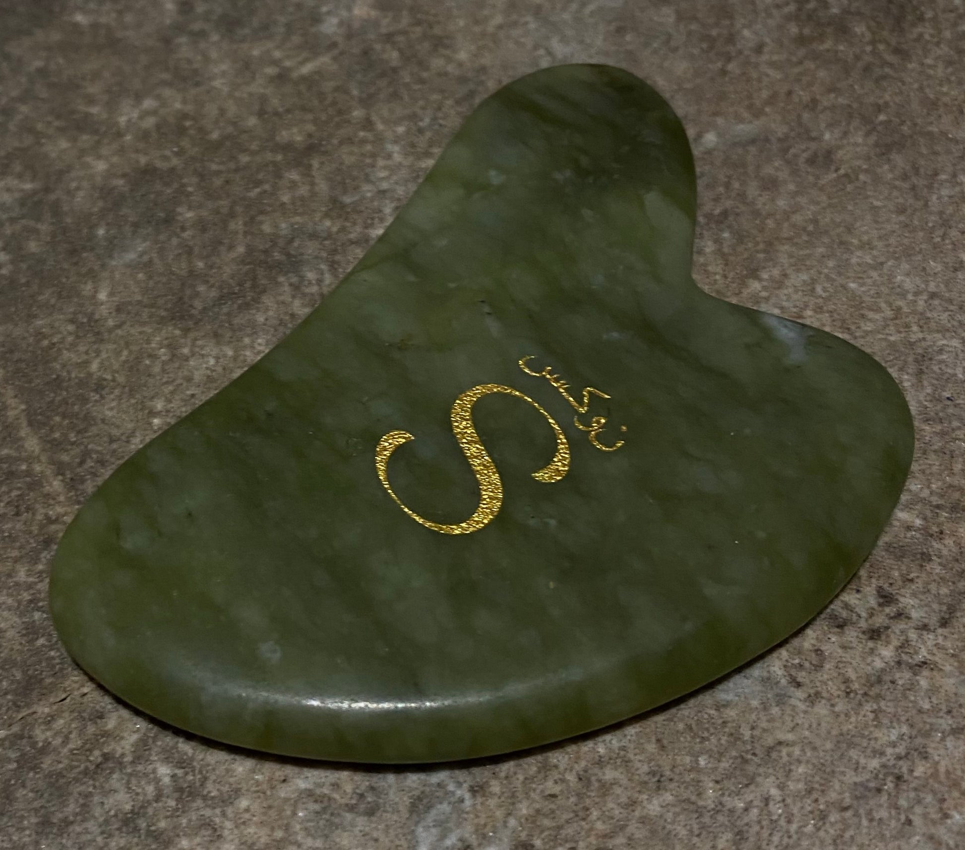 Green stone tool with gold 'S' logo on a brown surface