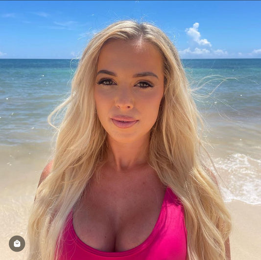 Woman with long blonde hair wearing a pink top on a beach with ocean in the background