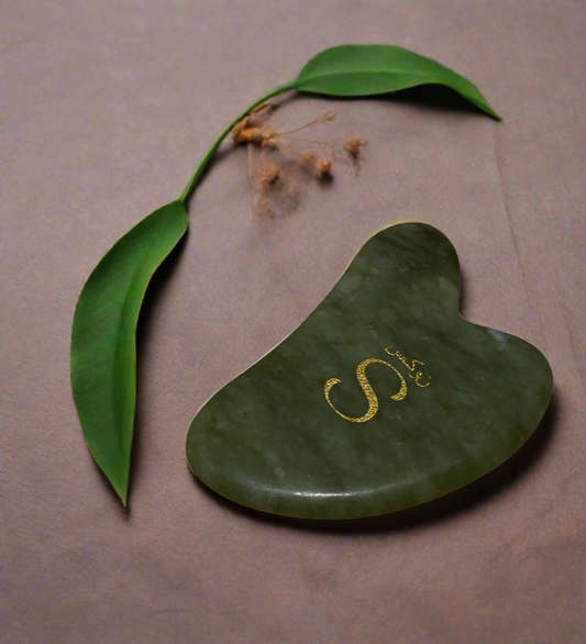 Green gua sha tool with gold logo on a brown background